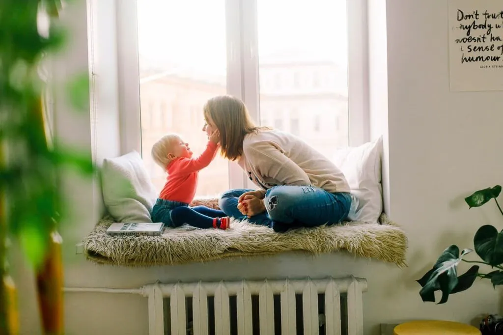 A woman sits on a window sill with a child